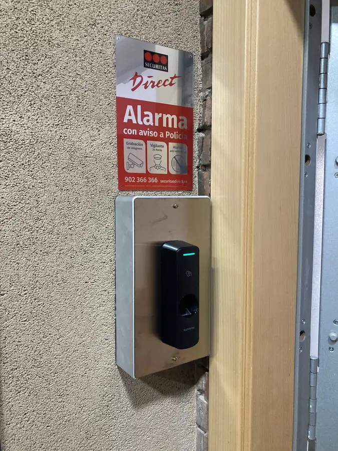 Lector biométrico de huella dactilar instalado junto a la puerta de una oficina para el control de accesos